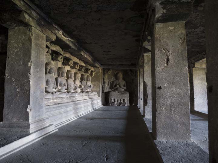 View along front wall with figure of seated Buddha at end of side wall, Ellora Cave 12 thrid floor
